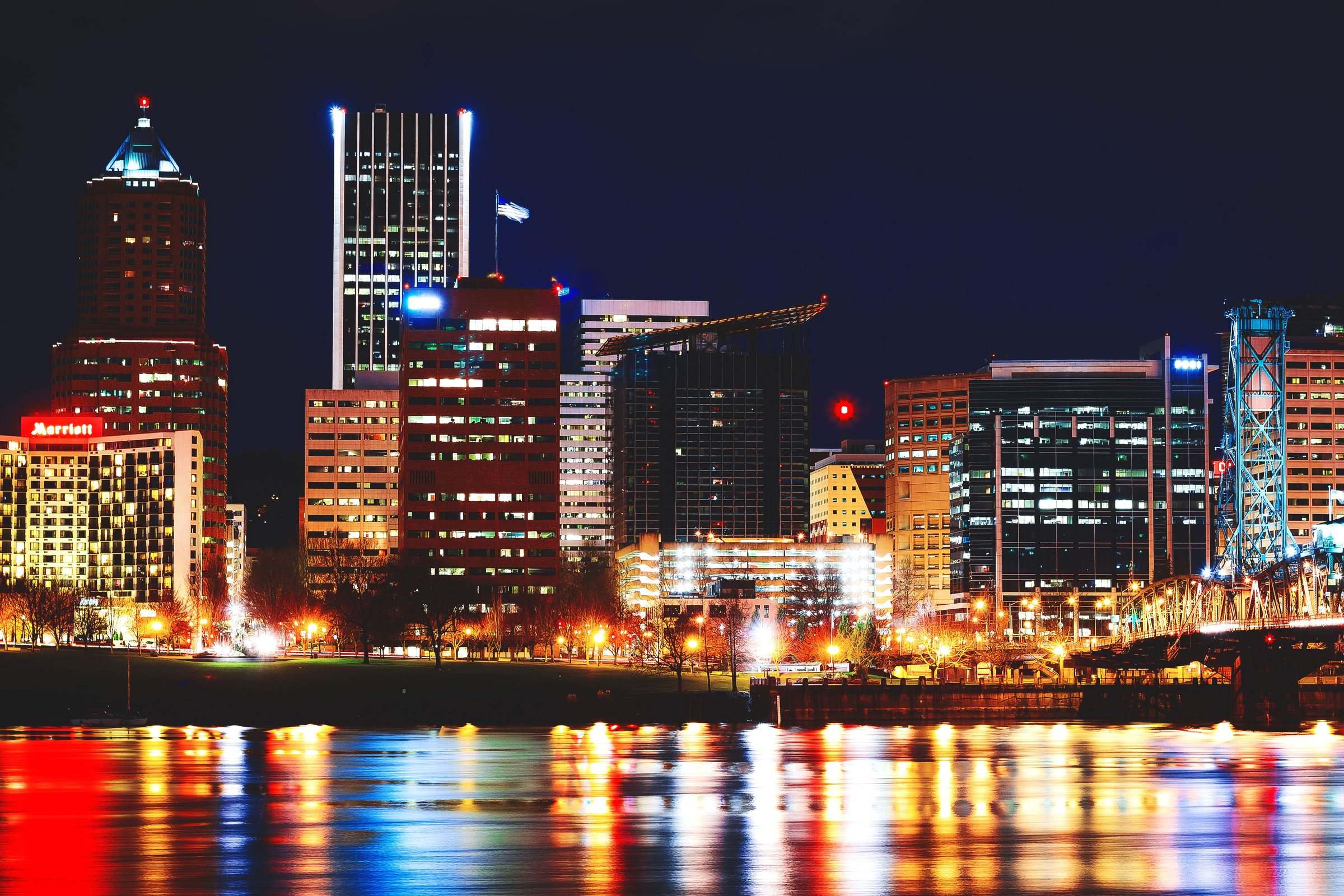 Downtown Portland's skyline lit up at night, reflected in the Willamette River