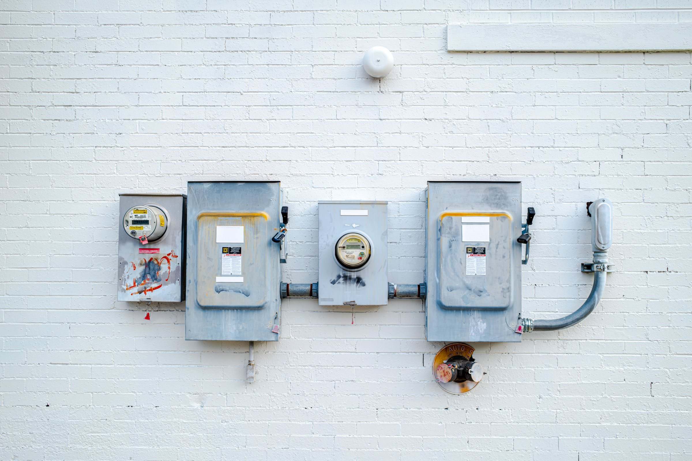 Electric meters and disconnect boxes mounted on a white brick wall