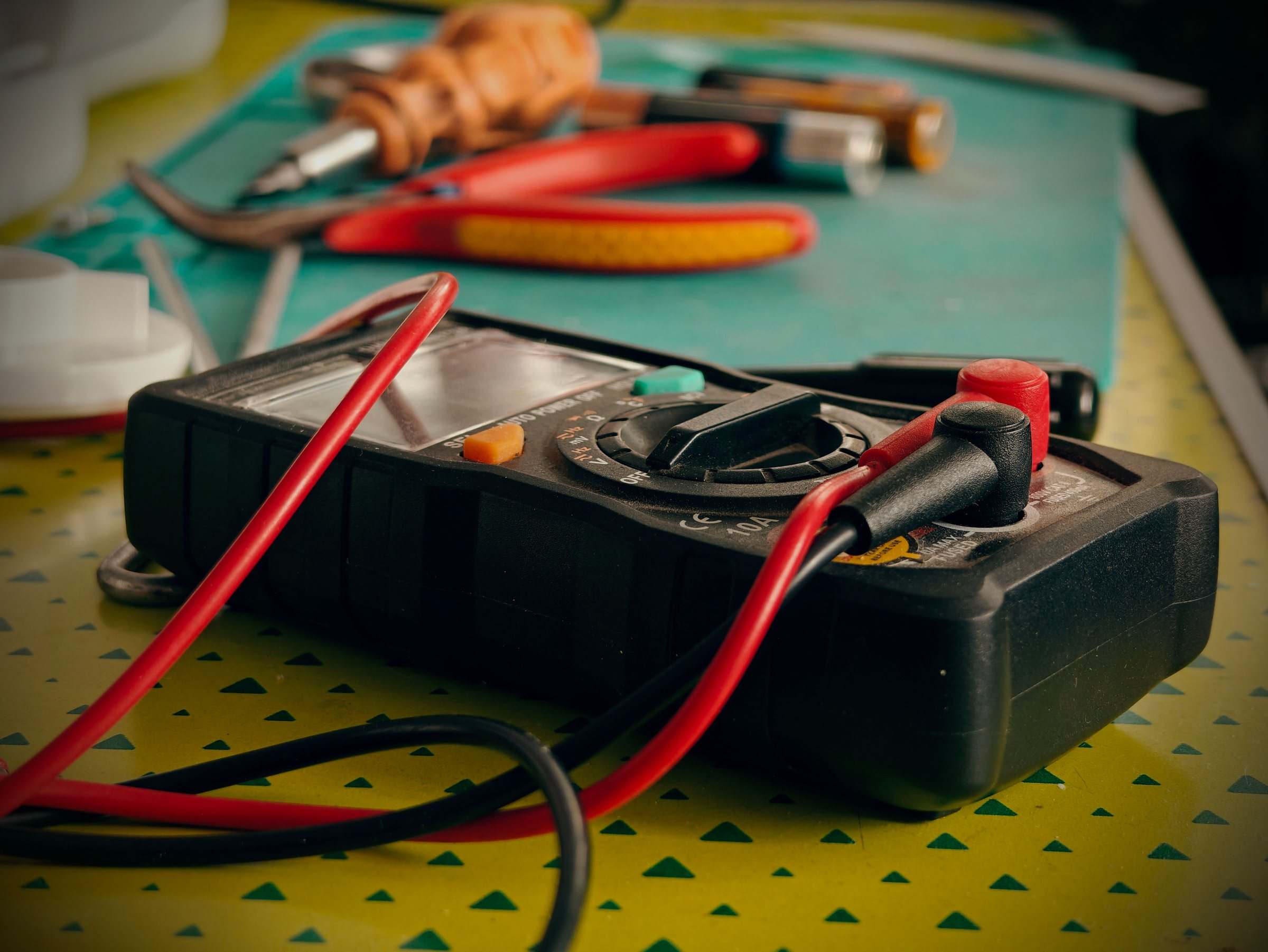 A multimeter and electrician's hand tools on a workbench