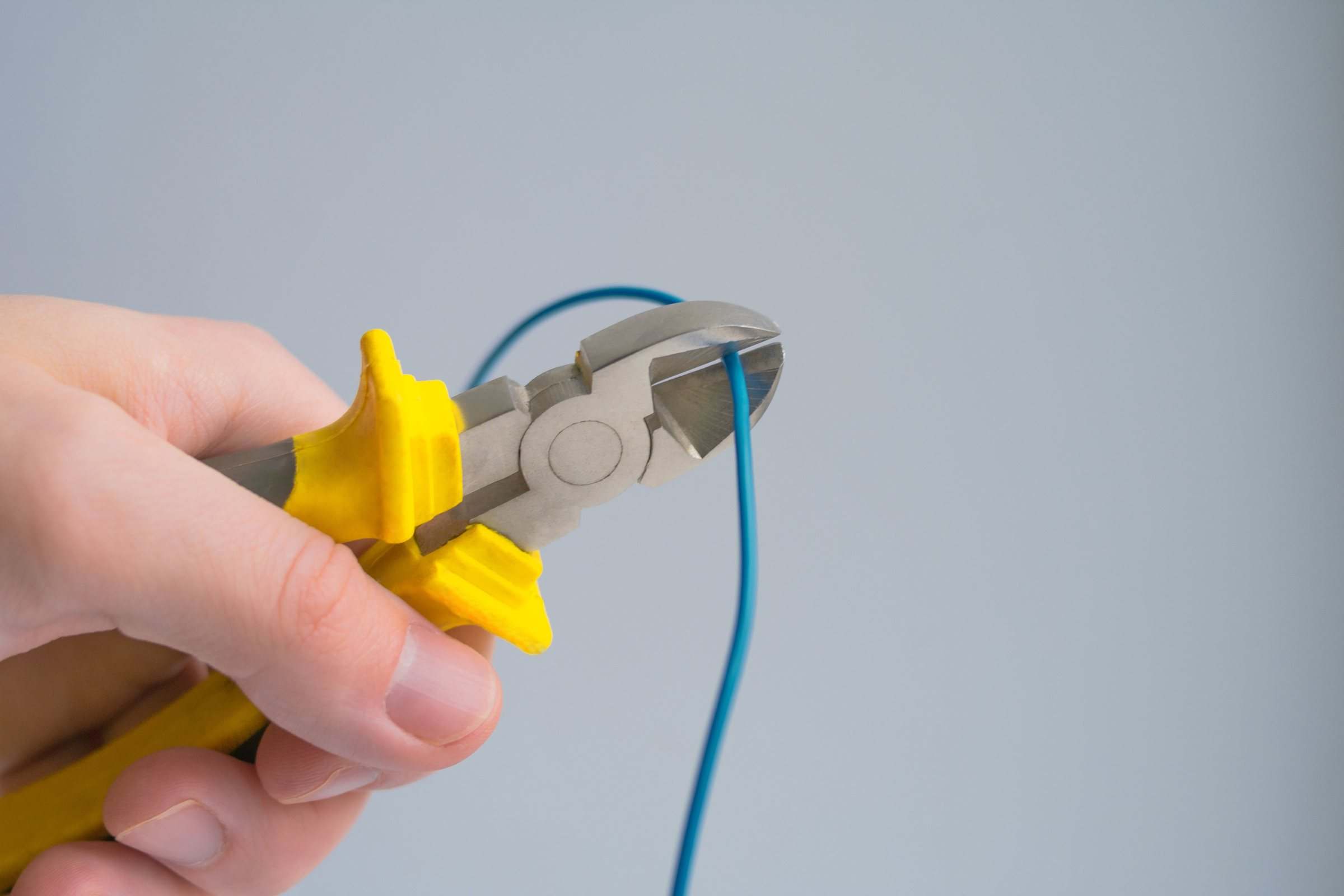 A hand using pliers to cut a blue electrical wire